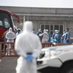Los pasajeros españoles que han abandonado el crucero (mono azul, gorro de plástico verde) reciben instrucciones de personal de la Unidad Militar de Emergencias y del Servicio de Sanidad Exterior. EFE
