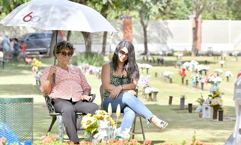 Dos mujeres colocan flores y velones en memoria de su padre fallecido.